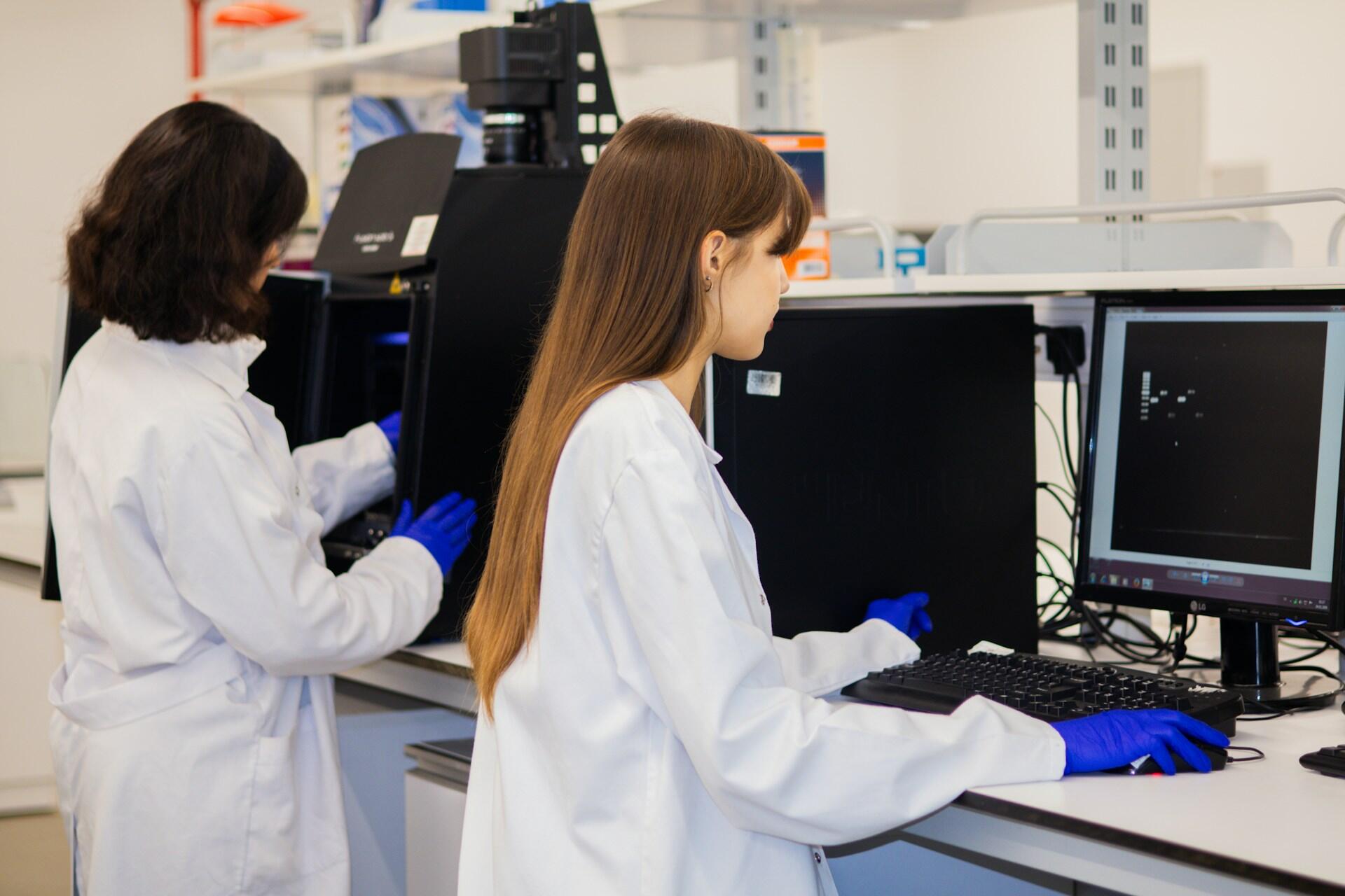 Dvi merginos laboratorijoje prie kompiuterių.