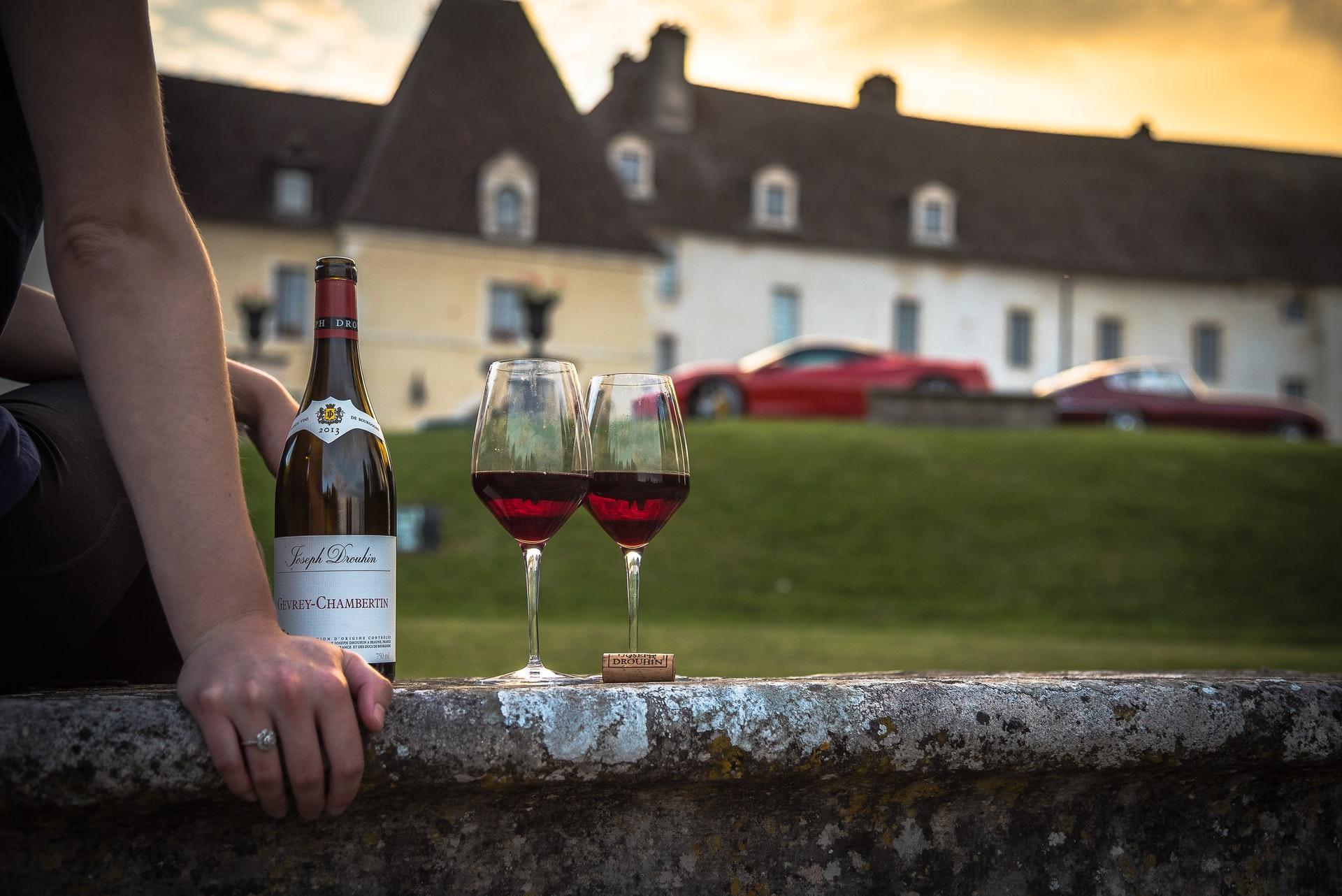 Une bouteille accompagnée de deux verres de vin rouge posés sur un muret