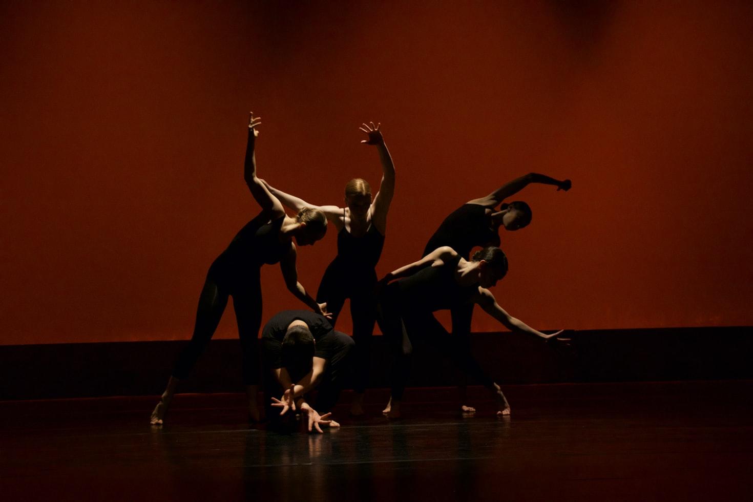 Danse contemporaine d'un groupe de femmes en justaucorps noirs, sous un spot de lumière avec un fond sombre et rouge.