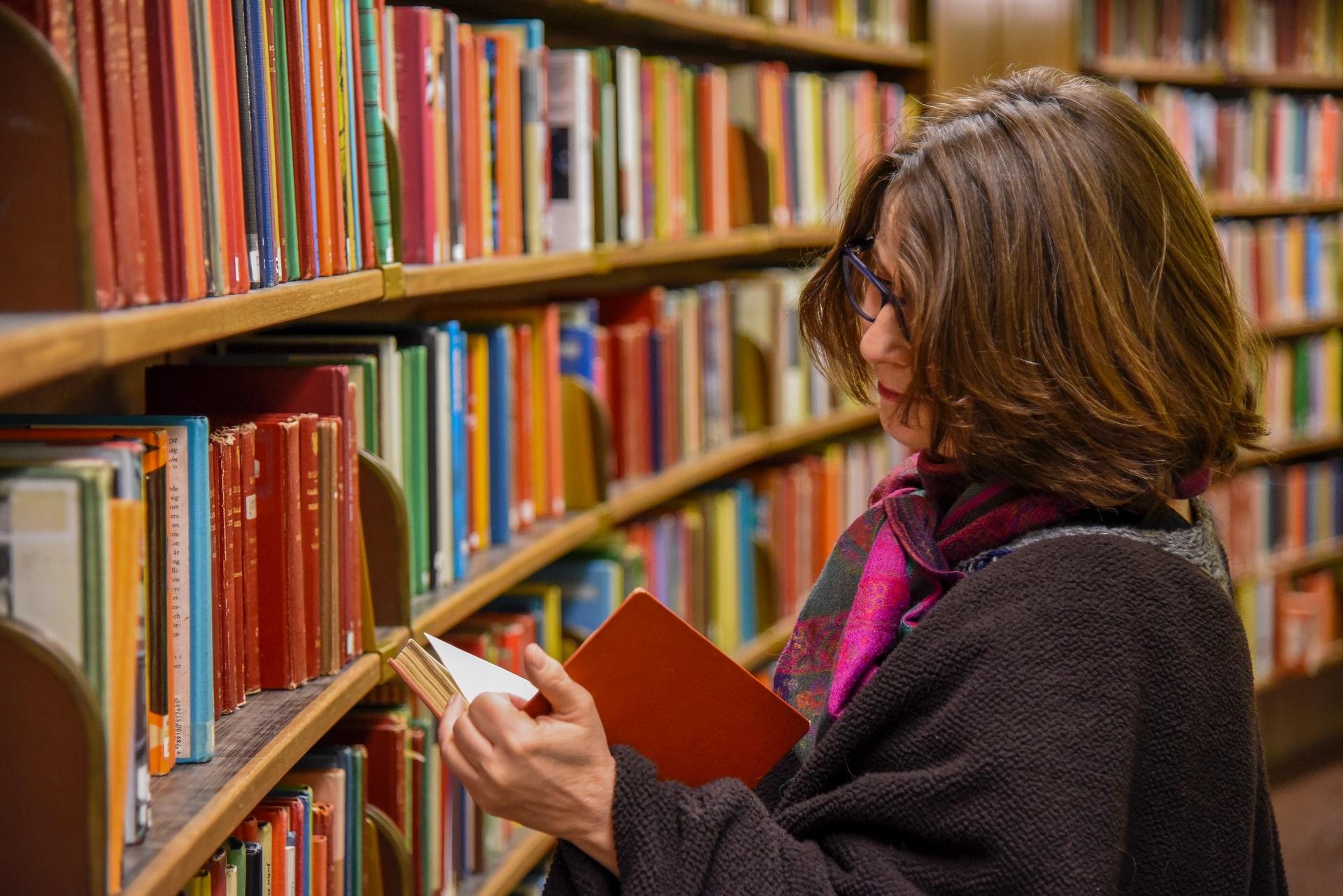 femme à lunettes ouvrant un livre dans une bibliothèque