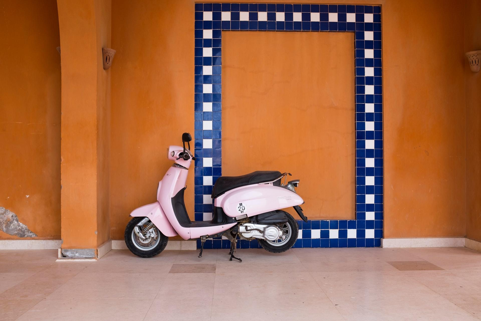 Scooter Vespa rose devant mur orange et cadre bleu