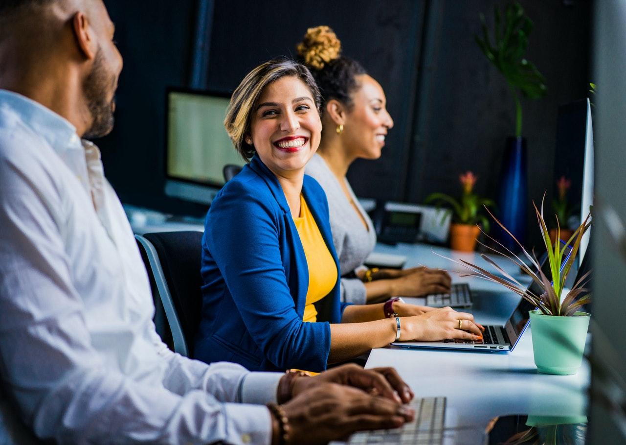 adultes en train de sourire pendant qu'ils travaillent sur des ordinateurs