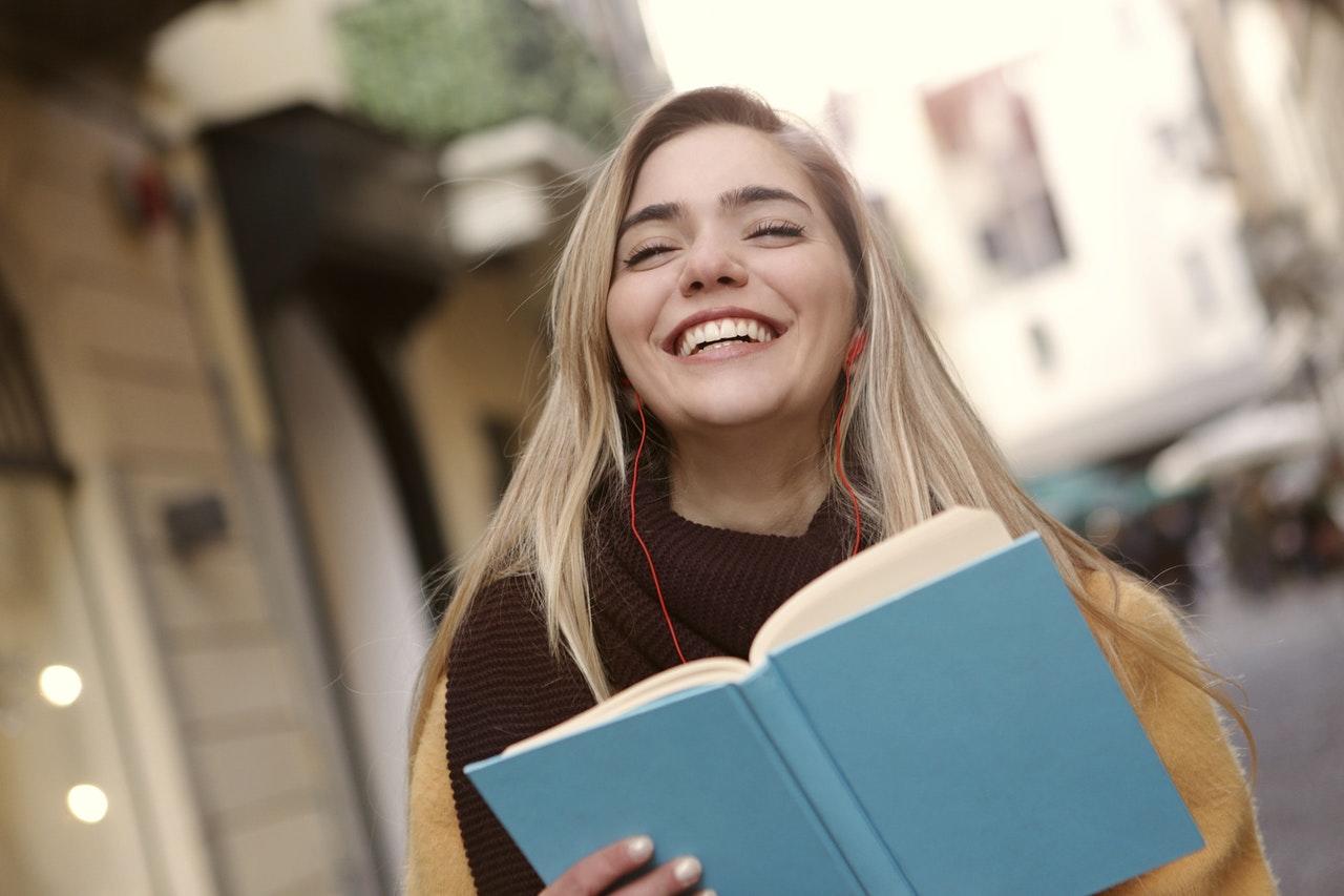 jeune femme blonde souriant dans la rue avec un libre bleu
