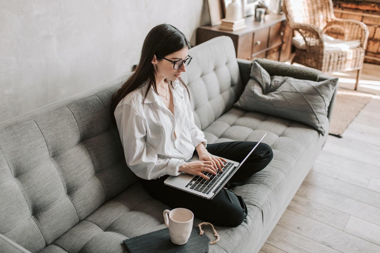 jeune femme brune a lunettes sur son canape travaillant avec son ordinateur et une tasse a cafe