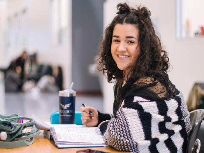 jeune femme très souriante en train d'étudier à une table