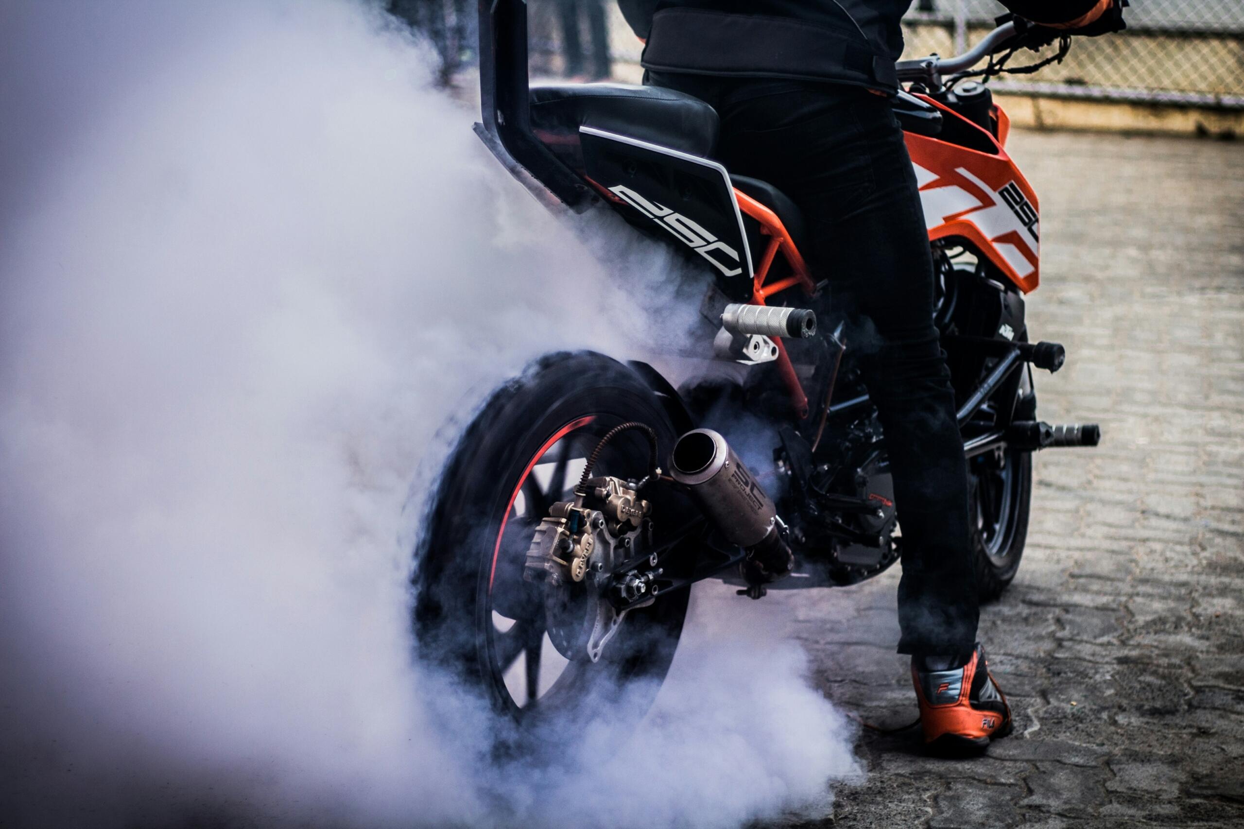 cilvēks uz motocikla un iedarbinātā motora izpūtes dūmu mākonis