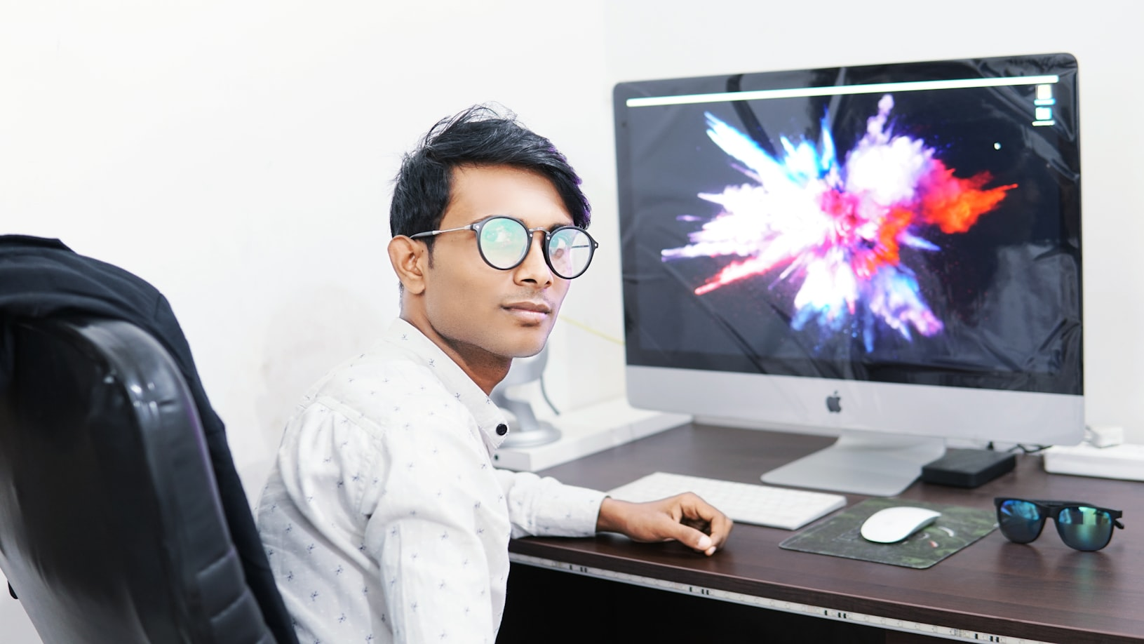 Jauns vīrietis, kurš sēž pie galda ar Apple iMac datoru