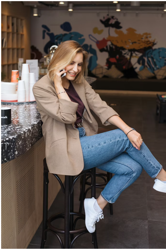 Sieviete, kas sēž kafejnīcā uz augsta krēsla, runā pa telefonu un smaida.