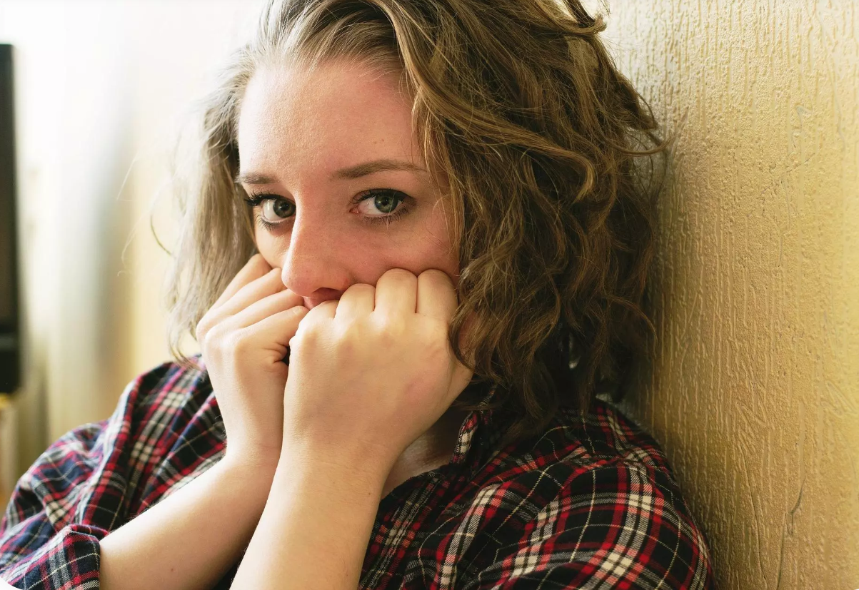 Jauna sieviete sēž pie sienas, satraukti saspiedusi dūres pie sejas.