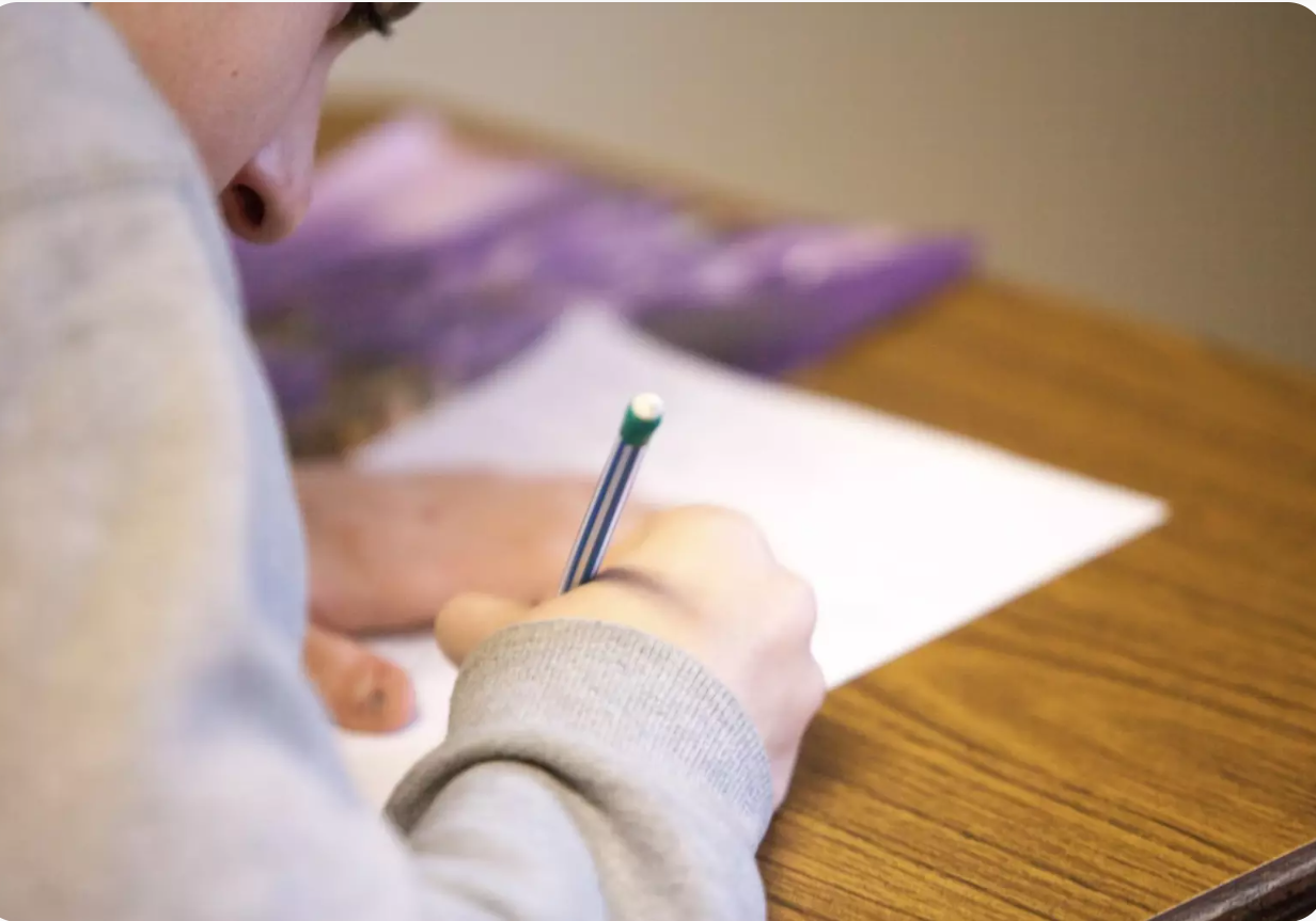 Skolēnu, kurš koncentrēti raksta uz baltas lapas.