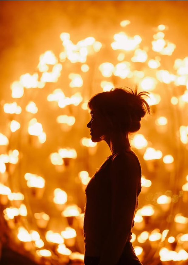 Sievietes siluets profilā liesmu gaismā.