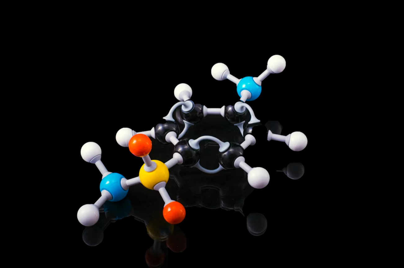 Krāsains organiskas molekulas 3D modelis ar gredzenveida struktūru uz melna fona.