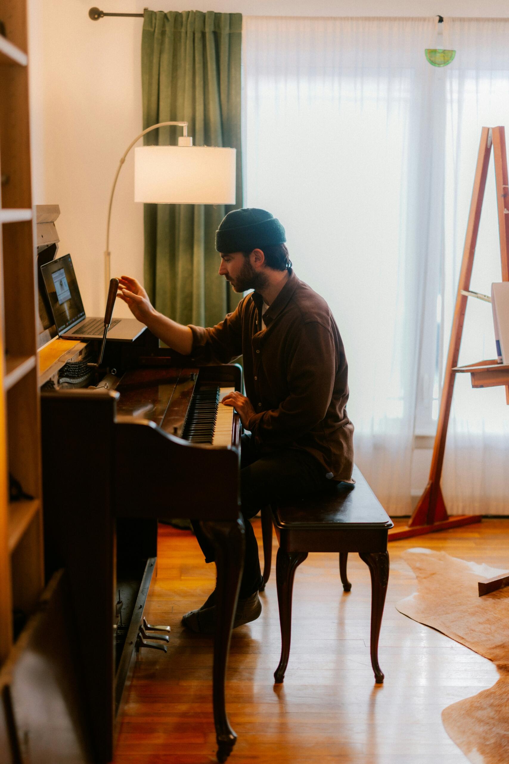 Cilvēks spēlē klavieres mājās, izmantojot digitālu ierīci mācībām vai notīm.