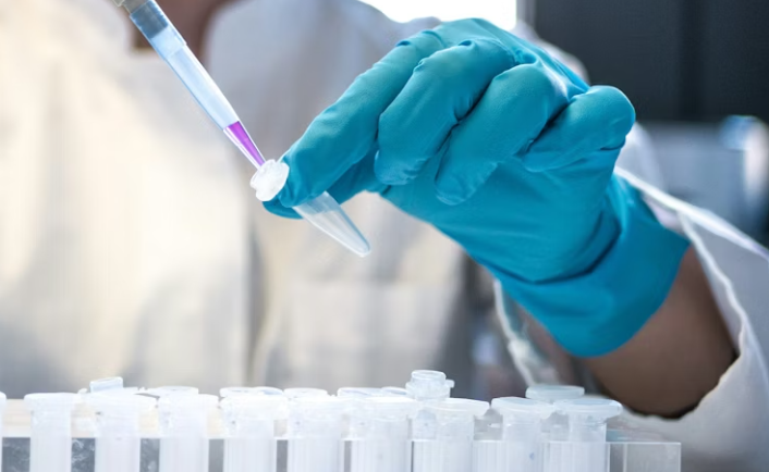 Laboratorijas darbiniece, kas ar pipeti dozē šķīdumu mēģenēs.