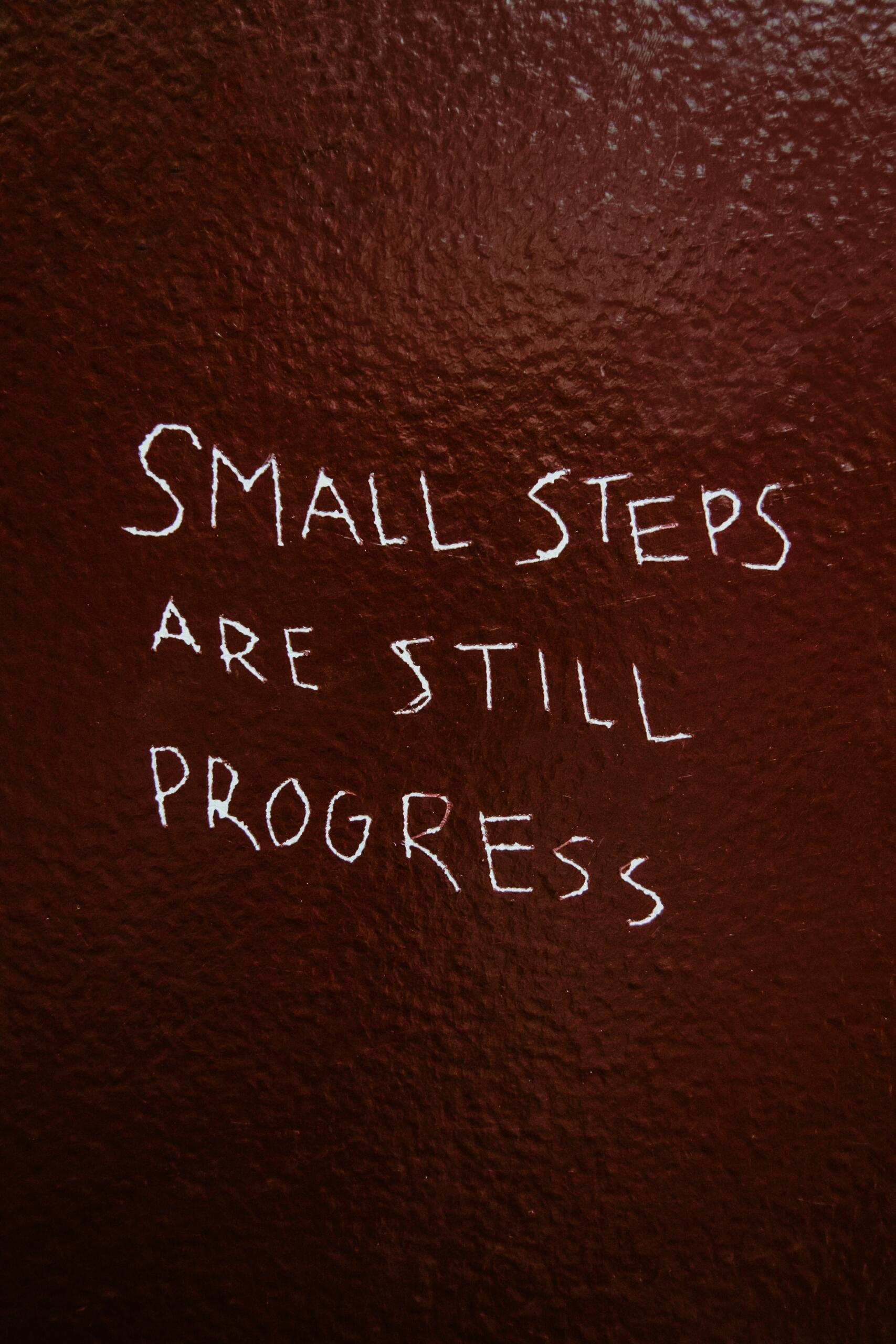 Uz sienas uzrakstīts motivējošs vēstījums “Small steps are still progress”.