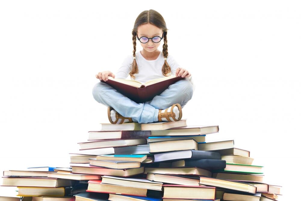 meitene lasa grāmatu, apsēdusies uz grāmatu kaudzes