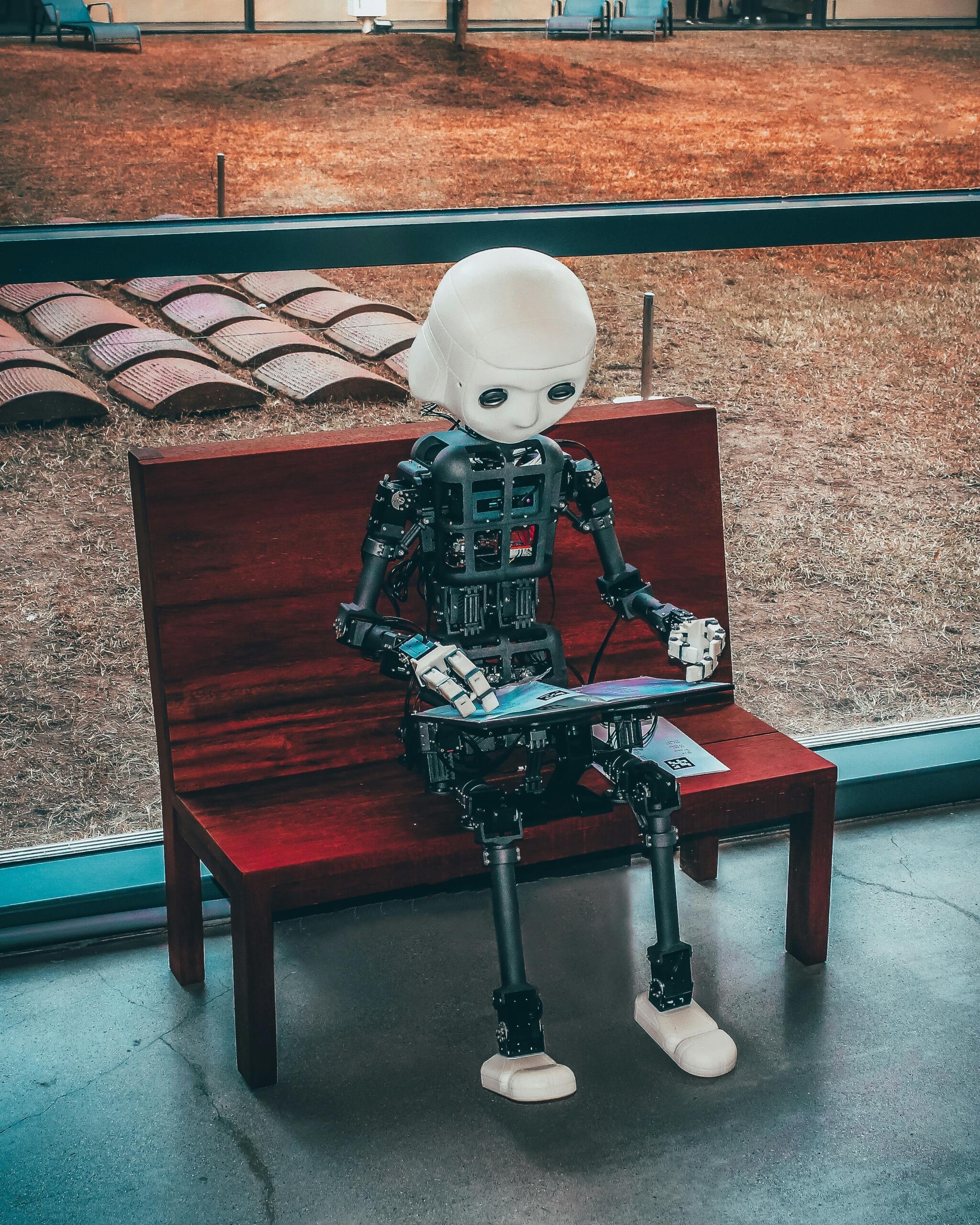 Robots sēž uz sola un izmanto portatīvo datoru.
