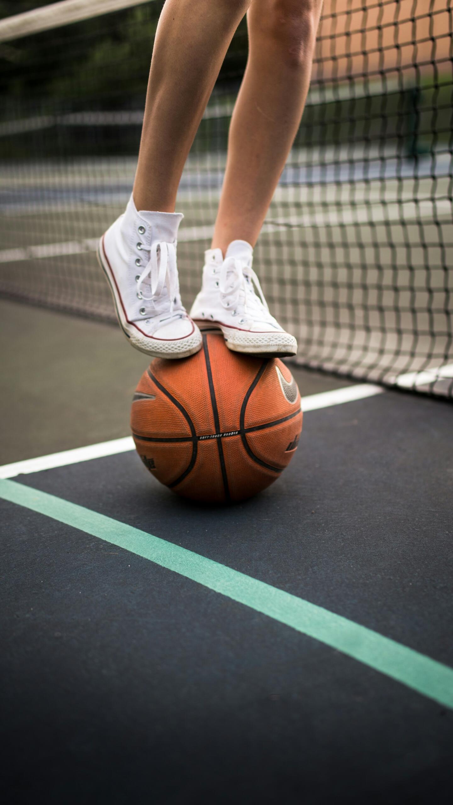 Cilvēks stāv ar kedām uz basketbola bumbas sporta laukumā.