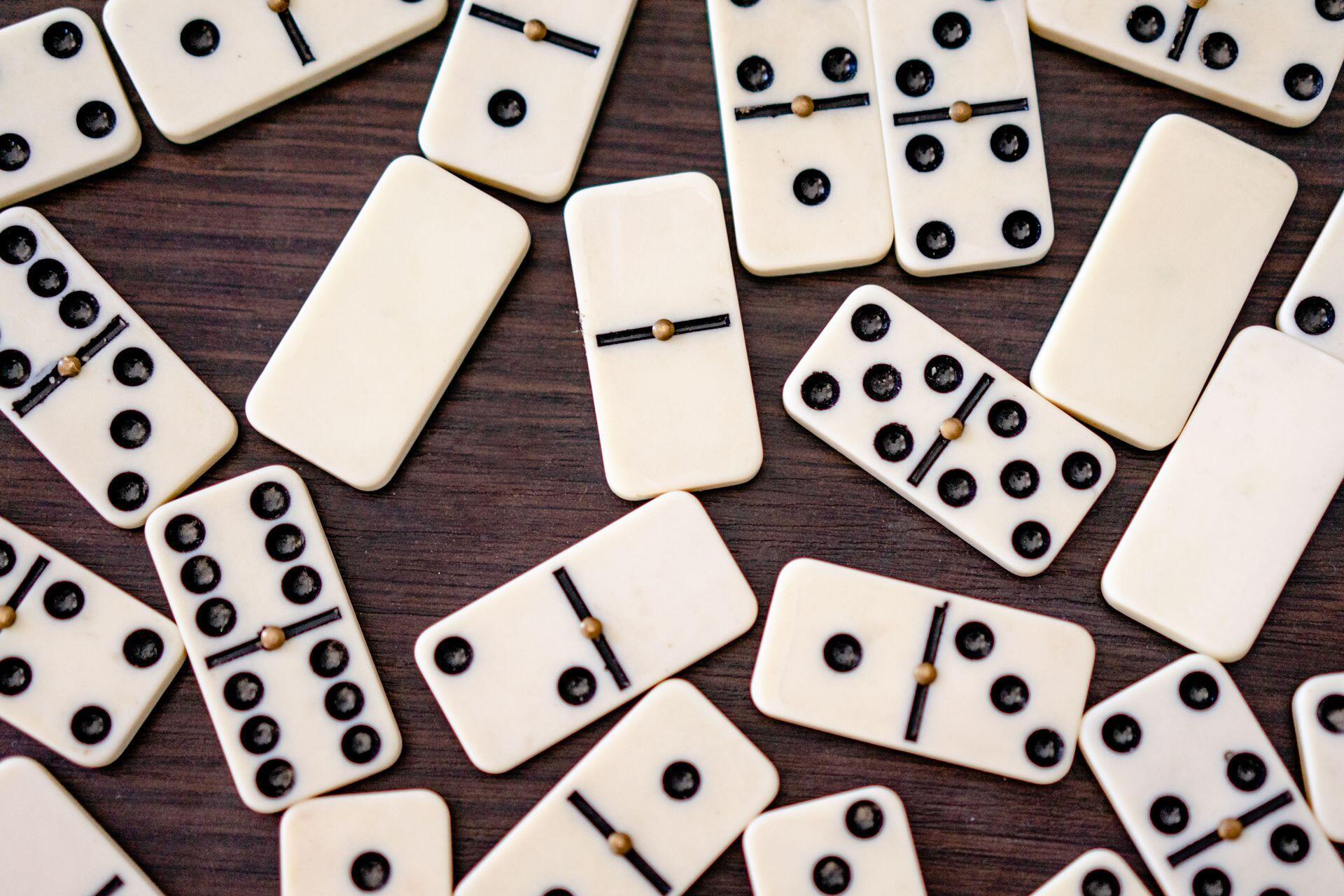 Scattered white domino tiles with black dots and wooden connectors on a dark wooden surface.