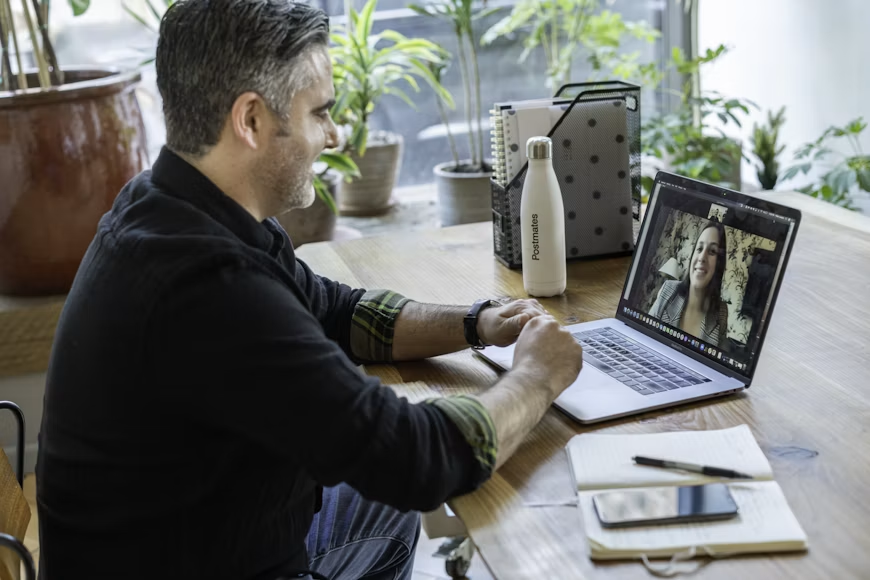 Muškarac u crnom džemperu radi u kancelariji koristeći laptop tokom virtuelnog poziva, što prikazuje savremeni način rada i komunikacije putem interneta.