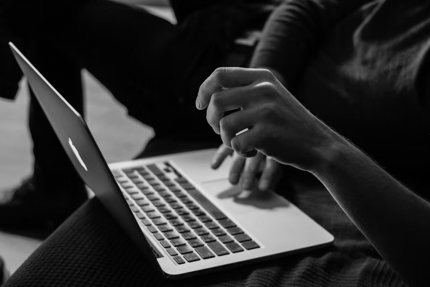 Crno-bijela fotografija osobe koja koristi MacBook, koja predstavlja savremeno učenje, rad i pristup obrazovnim sadržajima putem računara.
