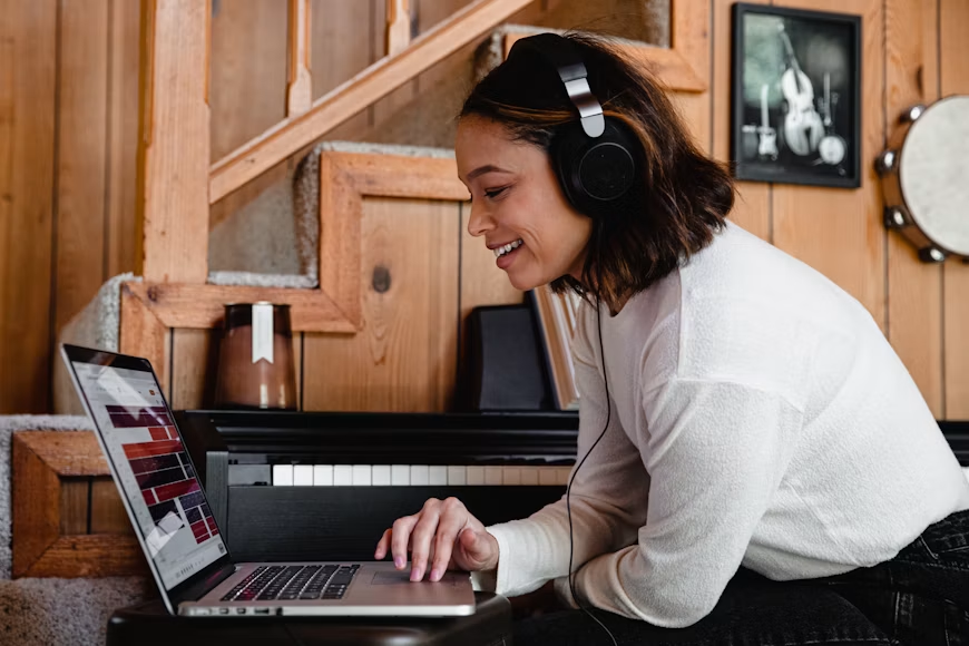 Žena u sivoj majici dugih rukava radi na MacBook Pro laptopu. Fotografija prikazuje savremeni rad na računaru i može se povezati sa učenjem, muzikom, kreativnim radom ili online časovima.