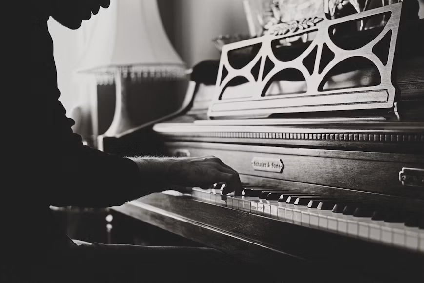 Krupni kadar muškarca koji svira spinet klavir, prikazan u crno-bijeloj tehnici. Fotografiija naglašava ruke, dirke i detalje klavira tokom sviranja.