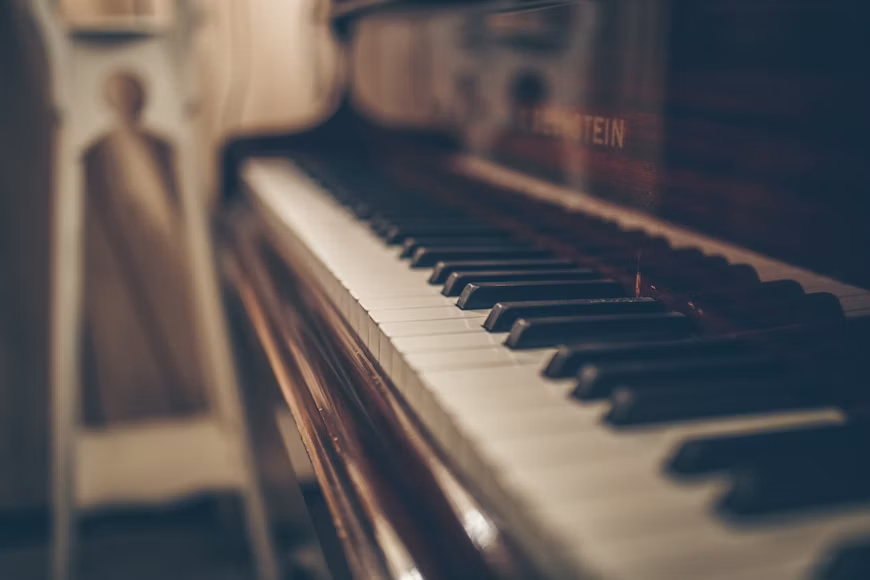 Krupni kadar klavira dok se u pozadini vidi osoba koja svira ili priprema instrument za sviranje.