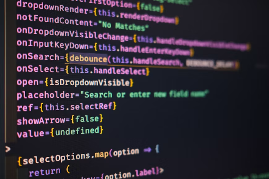 Krupni kadar ekrana laptopa koji prikazuje programsko okruženje sa tamnom temom i ispisanim Python kodom. Pozadina iza računara je potpuno neutralna i zamagljena, čime je cjelokupan fokus stavljen isključivo na programske linije koda na ekranu.