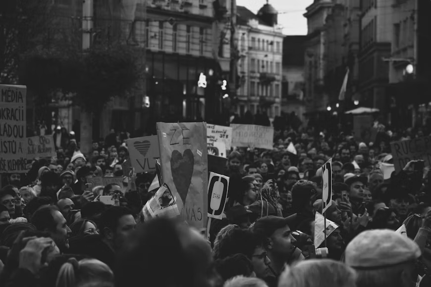 Upečatljiva crno-bijela fotografija velike mase ljudi koja sa transparentima i protestnim znakovima ispunjava gradsku ulicu. Snažan monohromatski kontrast naglašava energiju, odlučnost i zajedništvo okupljenih građana, čineći prizor savršenim vizuelnim prikazom društvenih promjena i građanskog aktivizma.