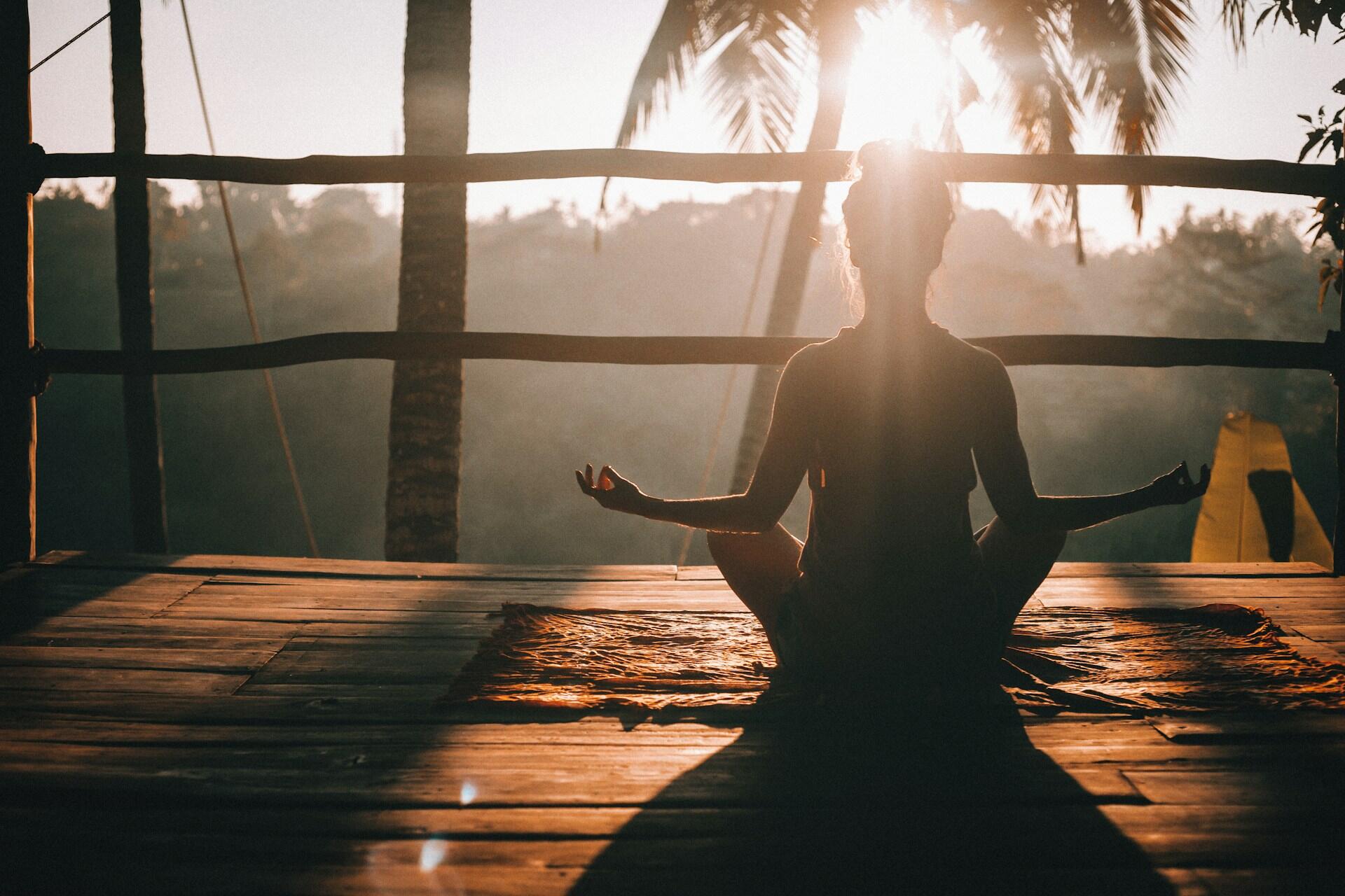 Person meditating in a cross-legged yoga pose at sunrise, representing the spiritual roots of yoga in ancient India.