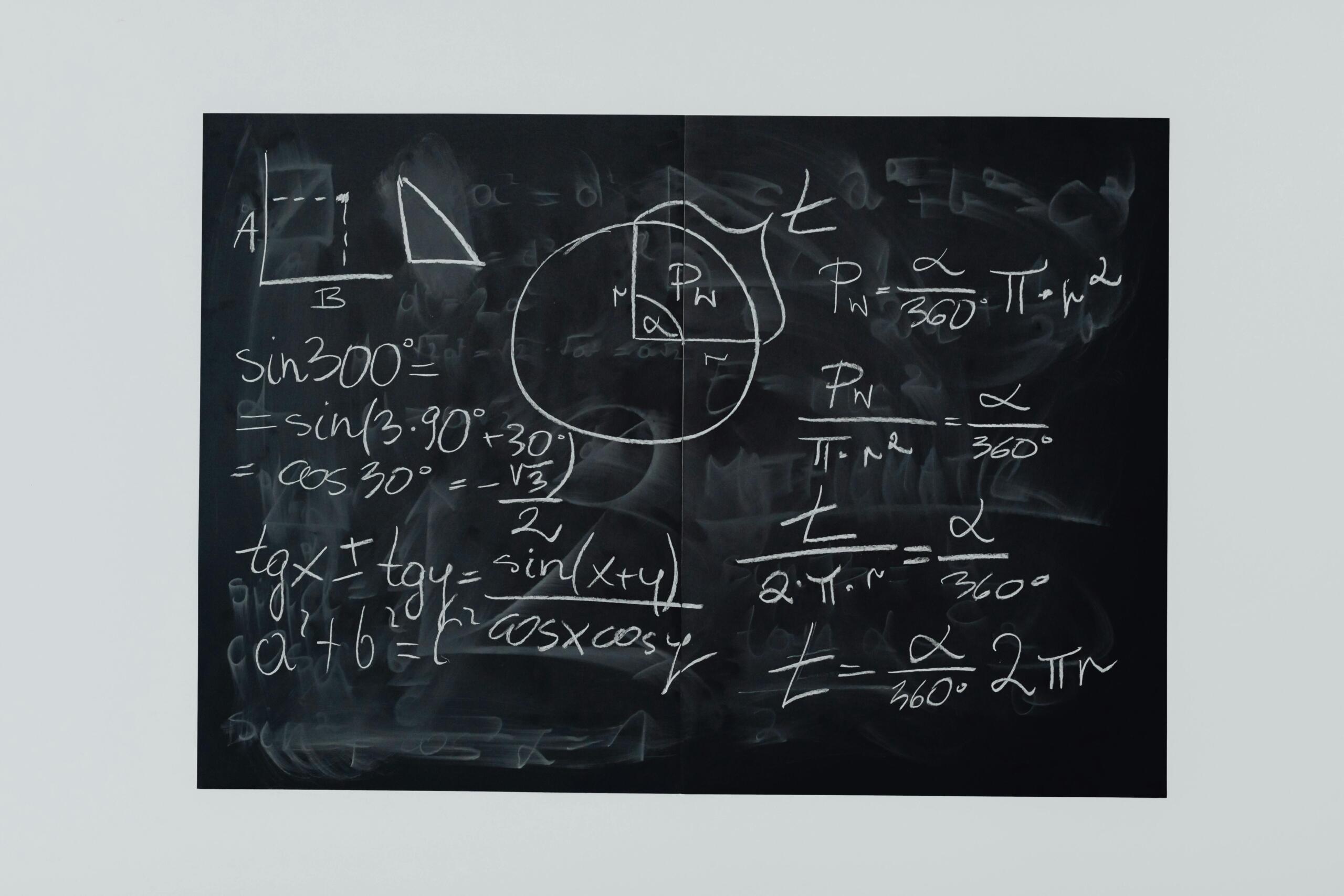 A black chalkboard on a white wall is covered with trigonometric equations, a sketch of a rectangle and triangle, a circle divided into sectors and handwritten formulas for sine, tangent and angles.
