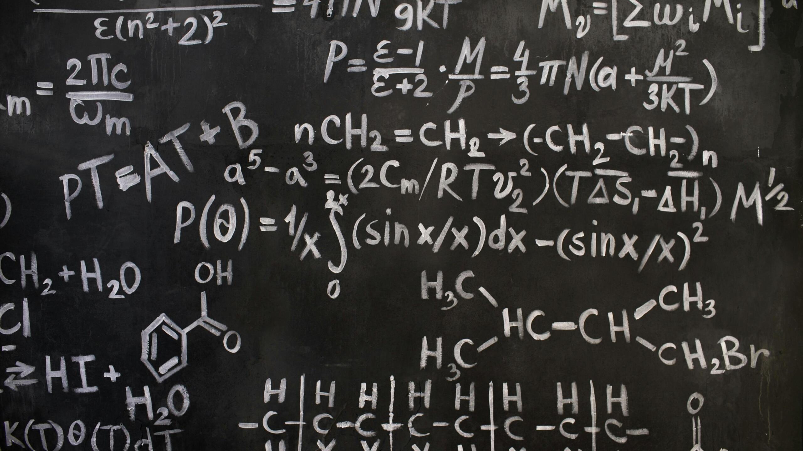 A chalkboard covered with complex mathematical and chemical formulas drawn in white chalk.