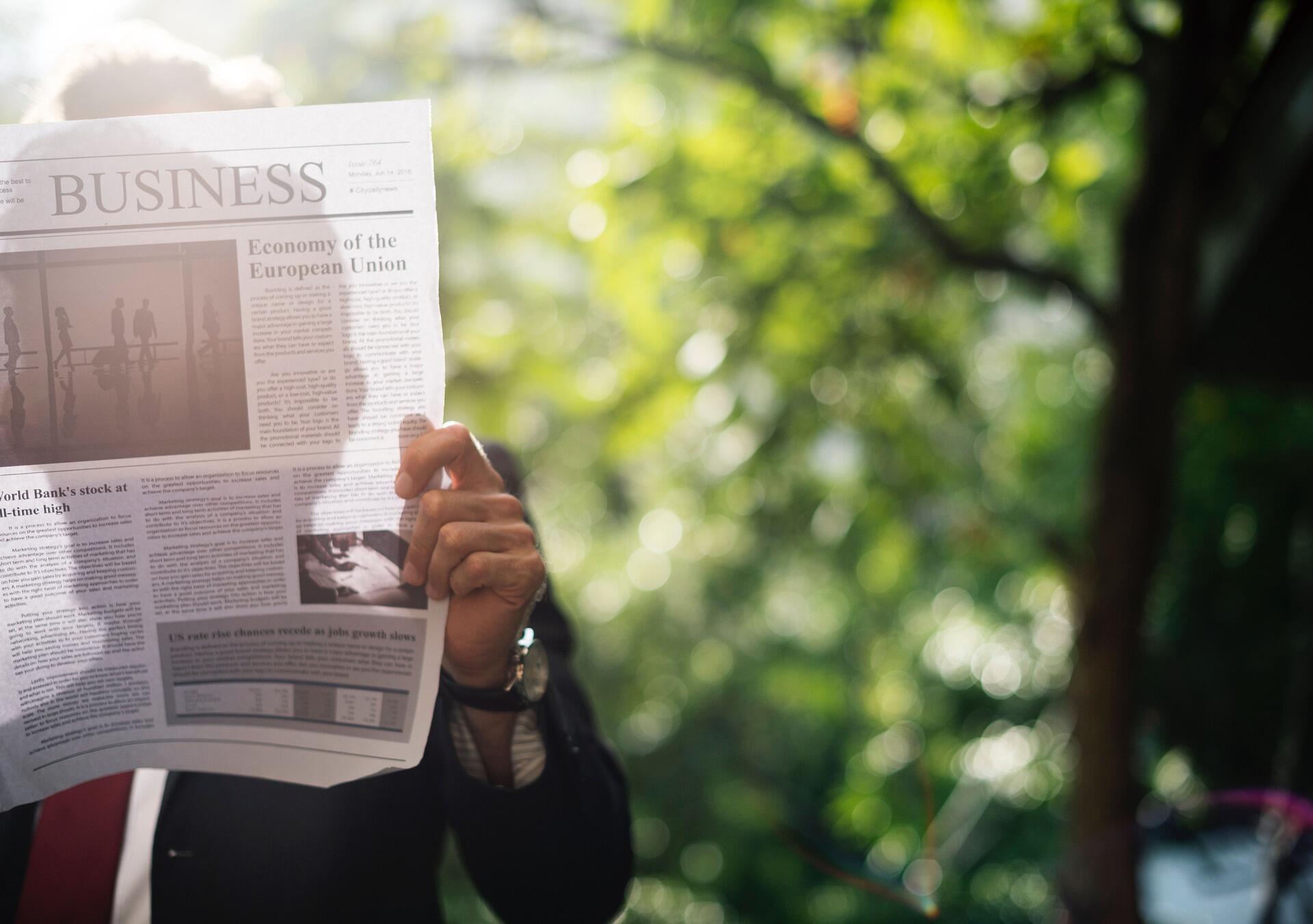 Person reading a business newspaper outdoors.