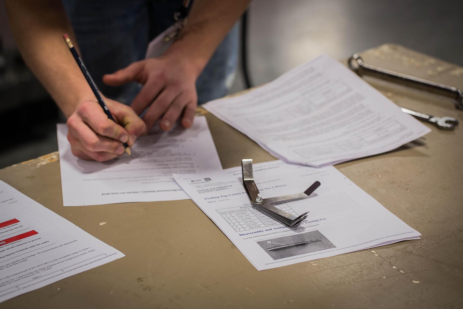 A person filling out paperwork on a workbench with scattered documents.