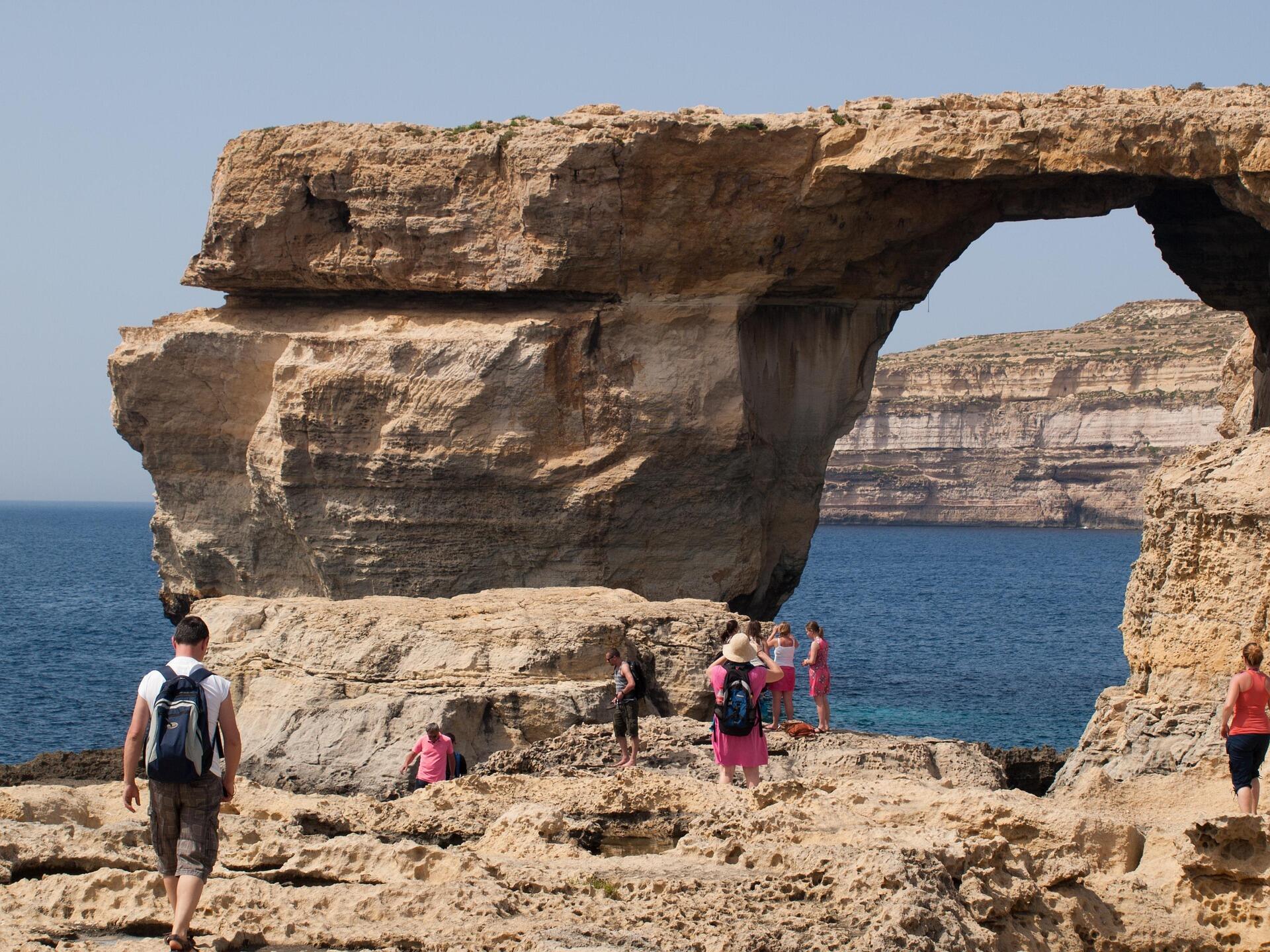 Tourists exploring the Azure Window rock formation on the coast of Gozo, Malta.