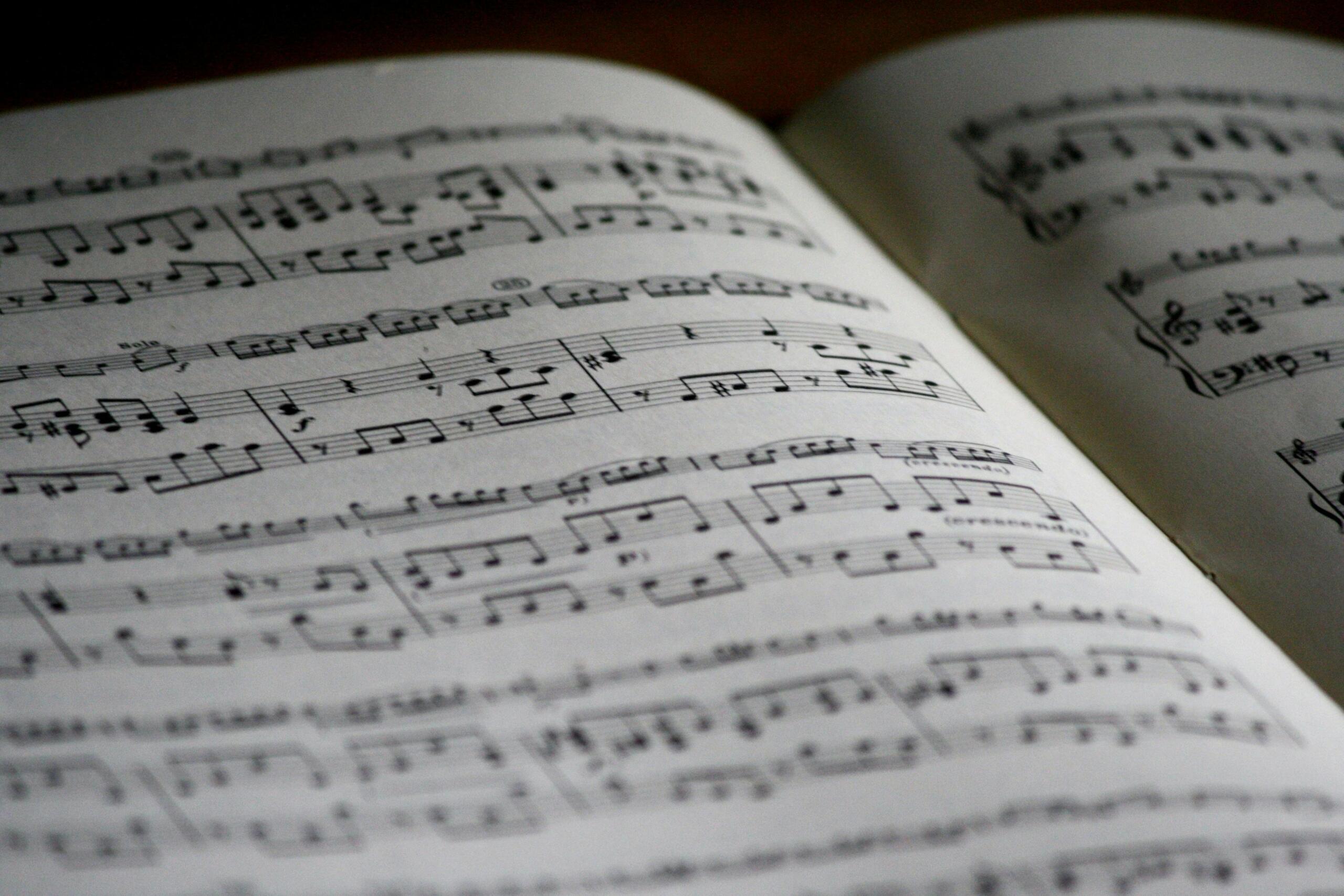 An open book of printed musical notation shows lines of notes and staves in sharp focus while pages curve toward the camera.