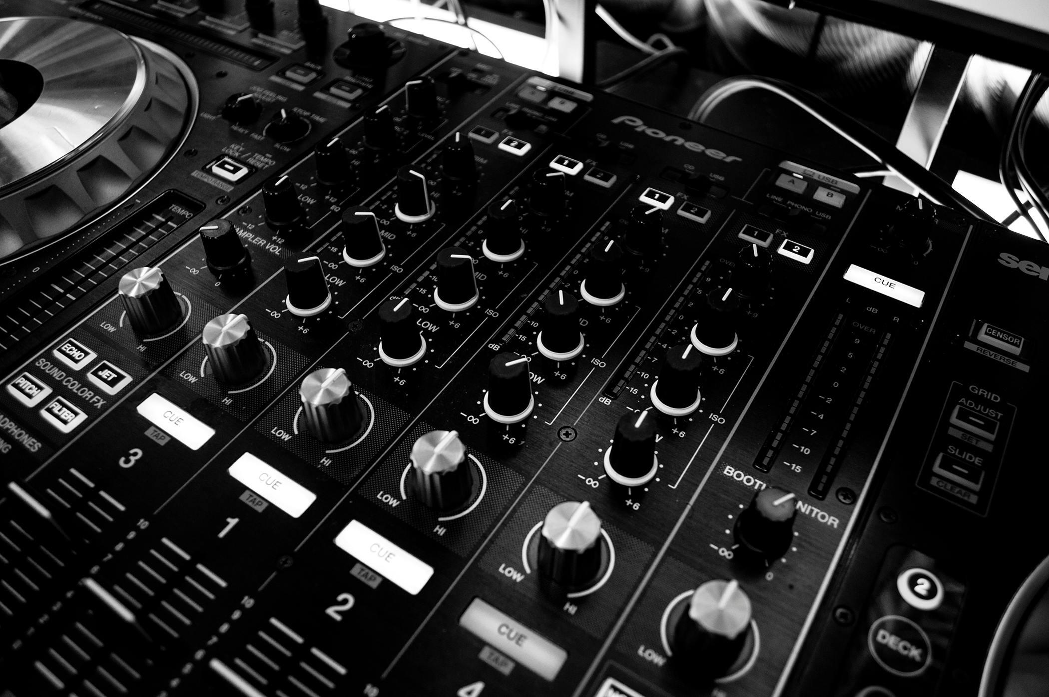 A close‑up black‑and‑white view of a DJ mixing console covered with knobs, faders and buttons.