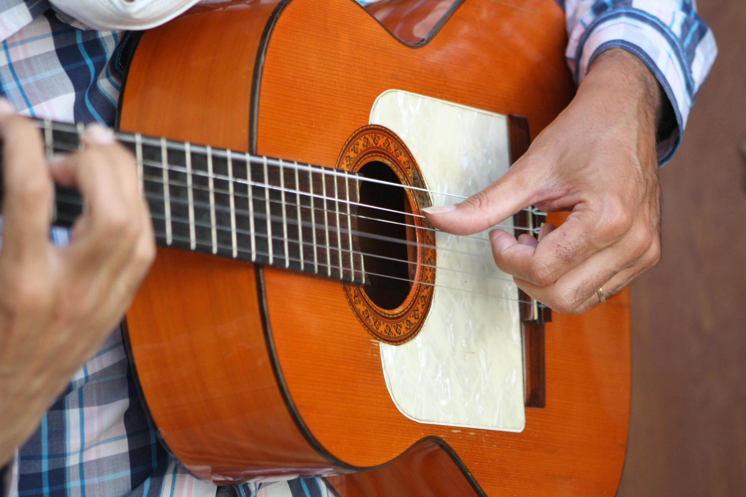 Close‑up of a musician’s hands strumming a wooden classical guitar, showing the rosette and refined finger movements.