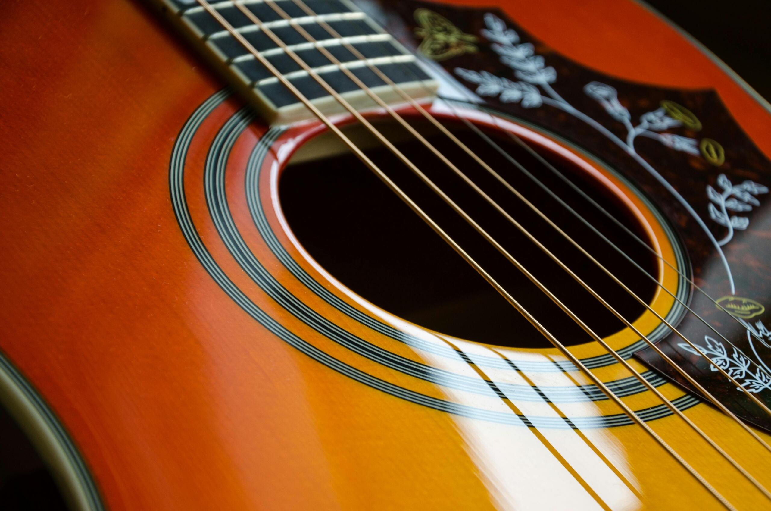 A close up of an acoustic guitar body, showing the soundhole, decorative rosette and strings in sharp detail.