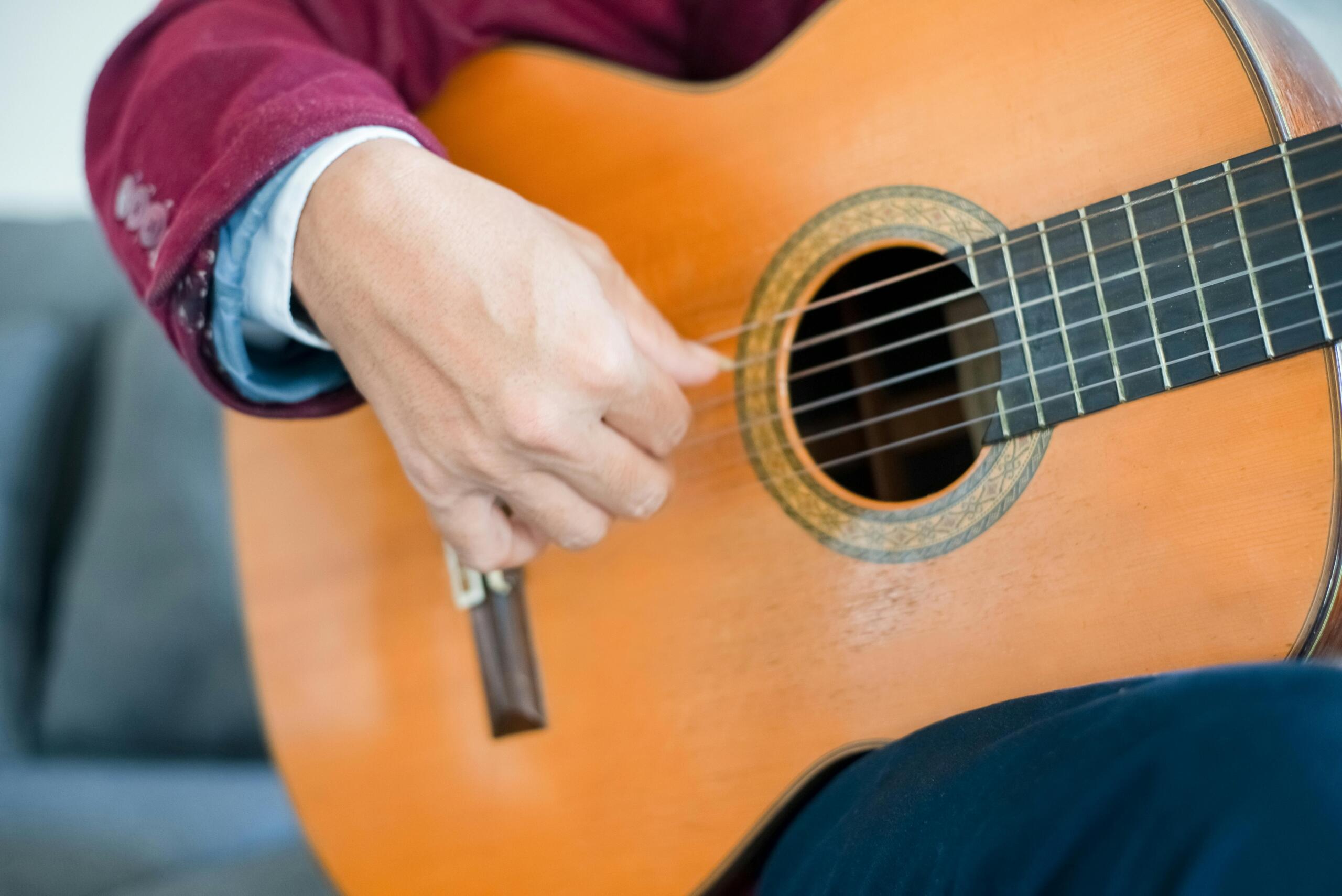 A close up of a hand plucking the strings of an acoustic guitar, with the instrument’s body filling most of the frame.