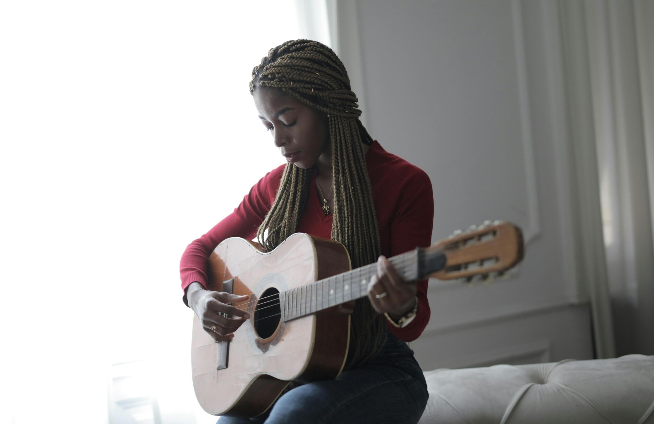 A person seated on a sofa, leaning slightly forward while playing an acoustic guitar in a bright living room.