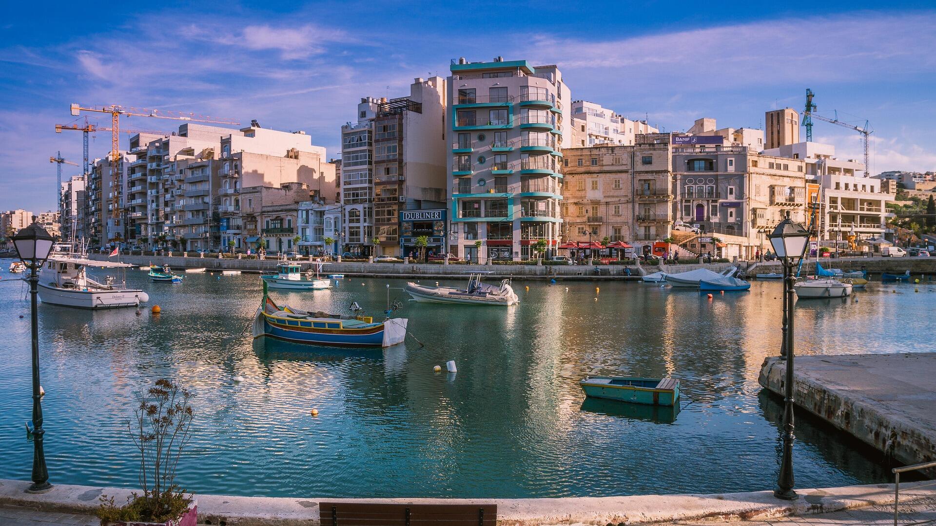 Colorful boats floating on calm water in a Maltese coastal town.