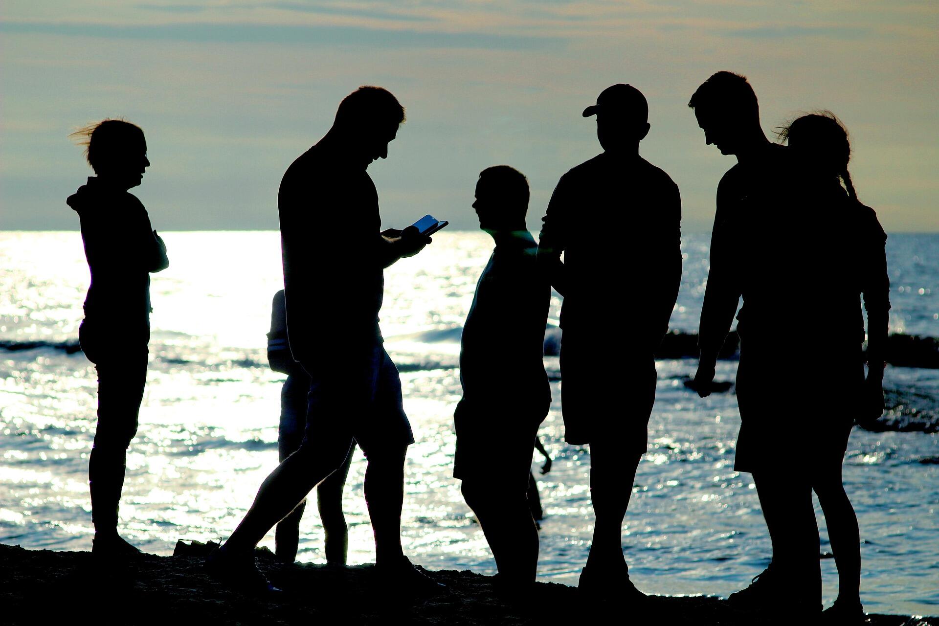 Silhouettes of people chatting by the sea at sunset, capturing a relaxed beach atmosphere in Malta