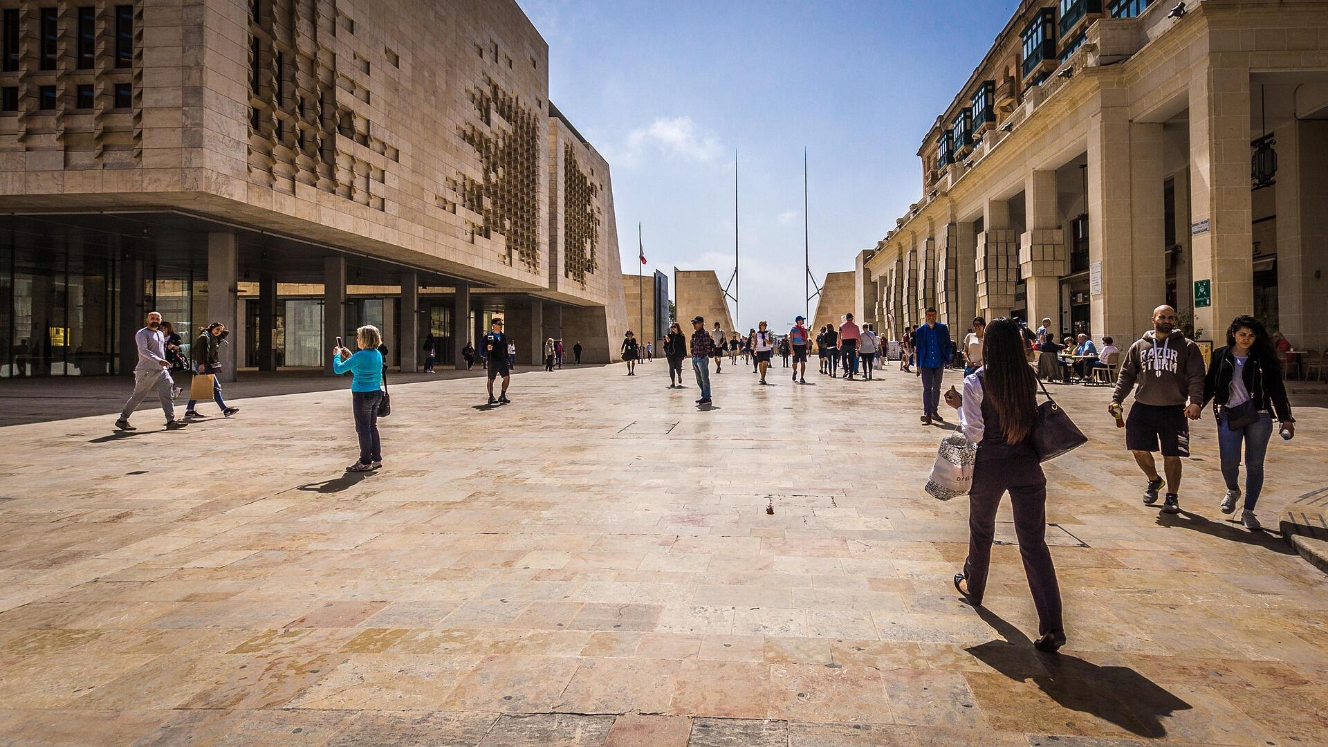 People walking through Valletta’s Parliament Square on a sunny day, surrounded by modern and historic Maltese architecture.