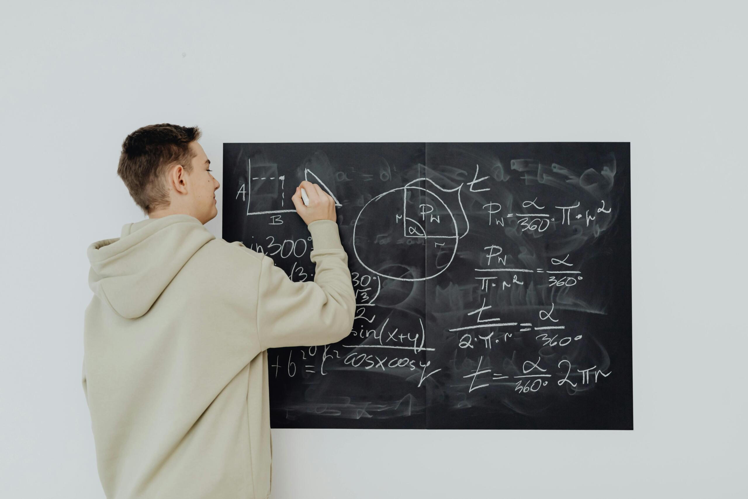 Student writing mathematical formulas and diagrams on a blackboard.