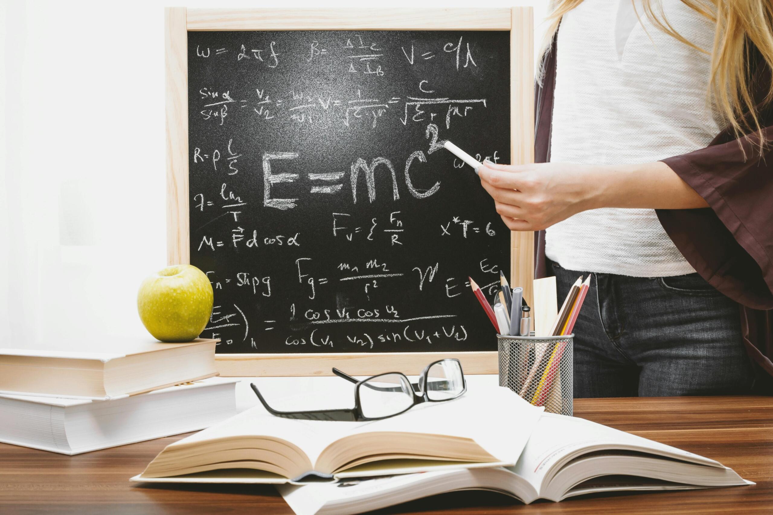Close up of a chalkboard covered with mathematical formulas next to open books and study materials.