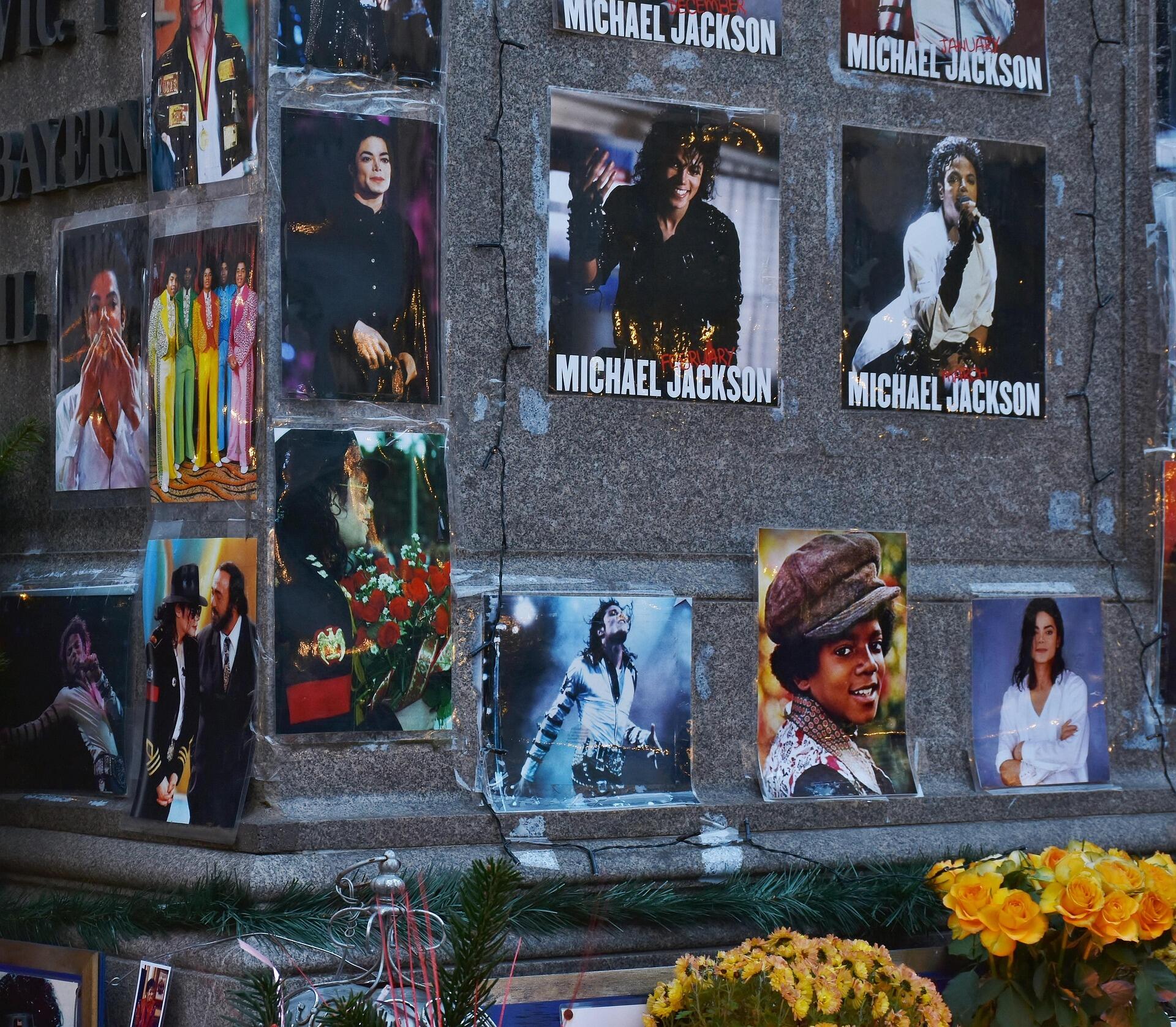 A public memorial shrine dedicated to Michael Jackson, featuring a collage of iconic photos and fresh yellow flowers left by fans.