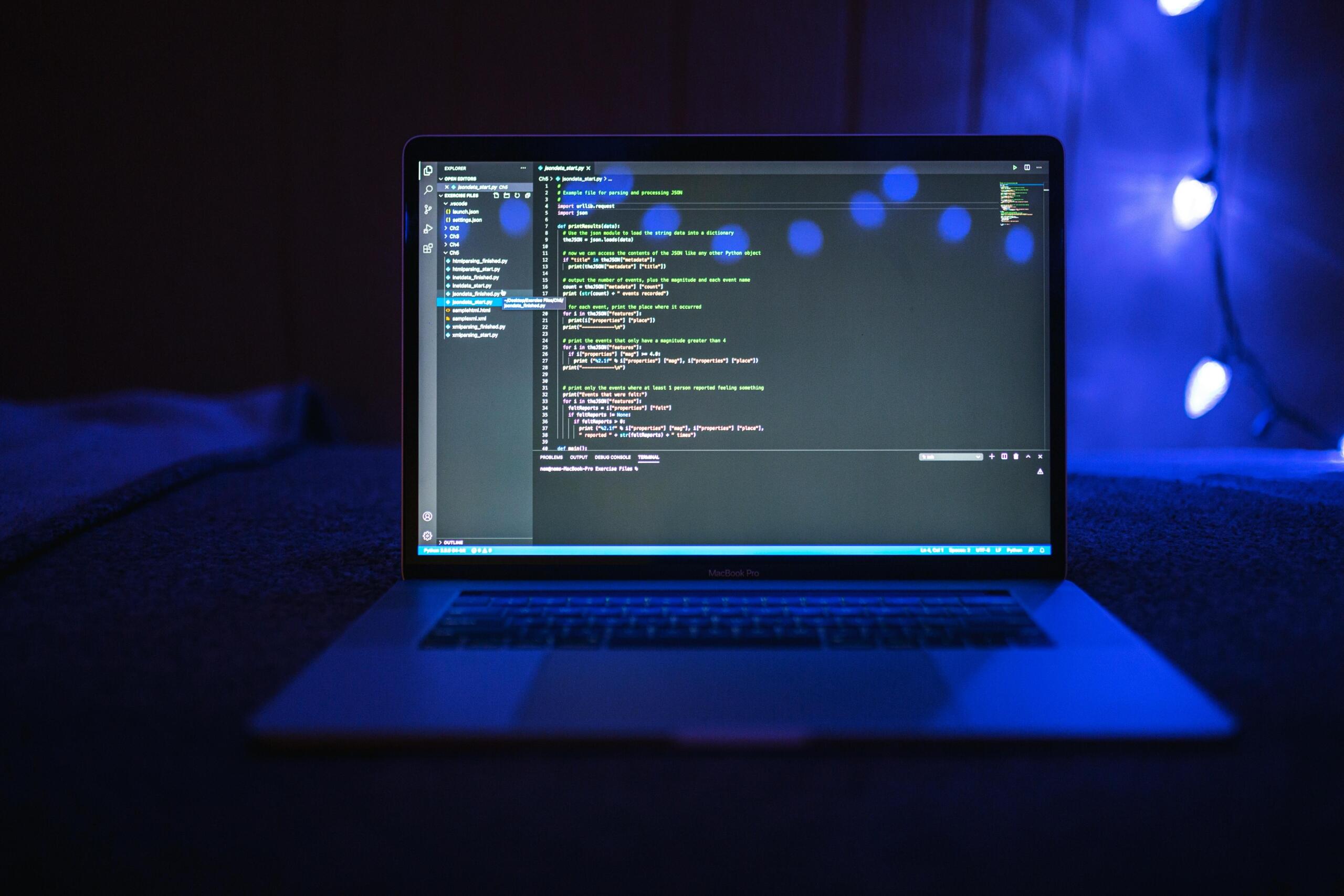Close up of a laptop screen displaying programming code against a dark background with blue lighting.