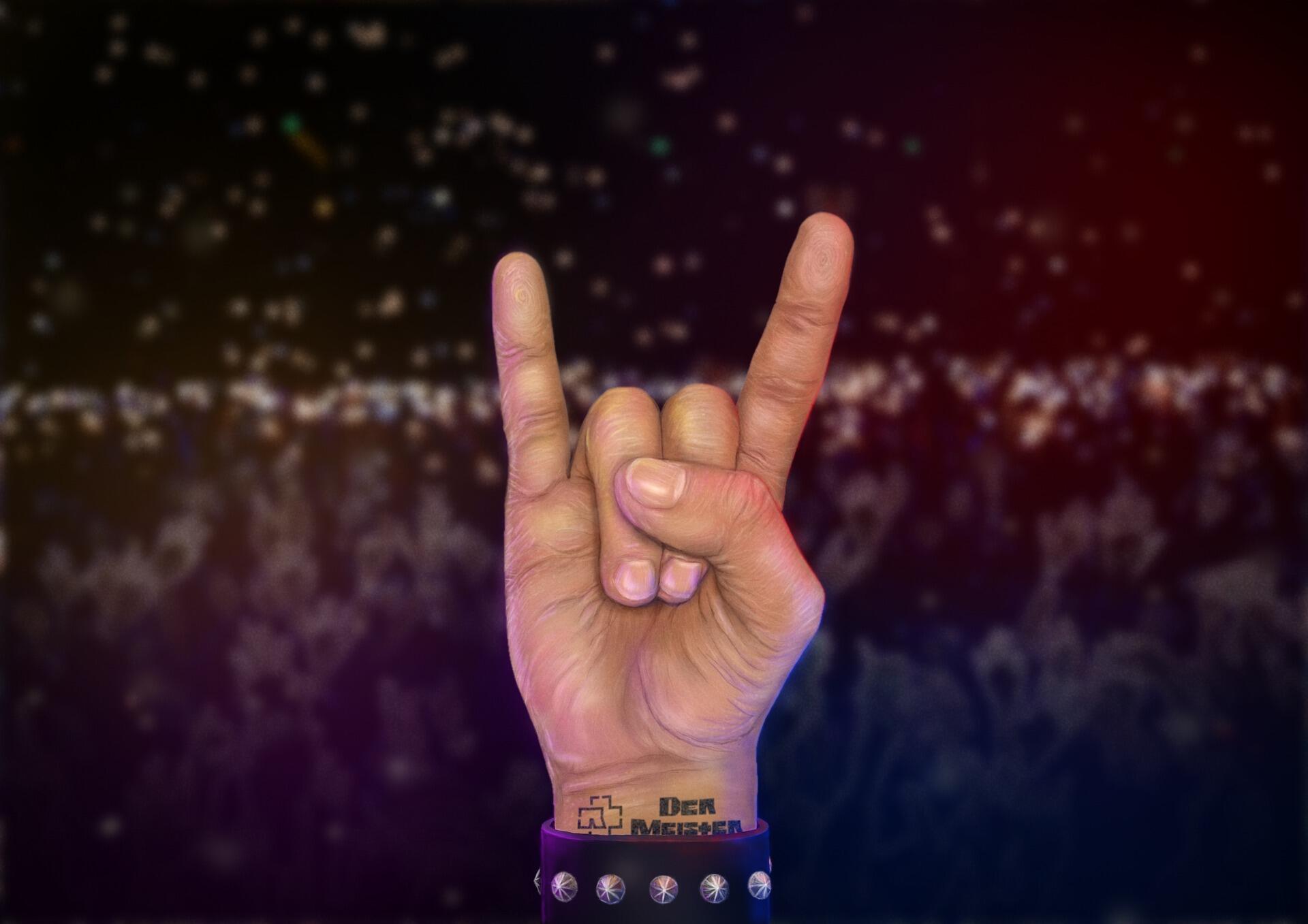 Hand showing the rock and roll sign against a blurred concert crowd at night.